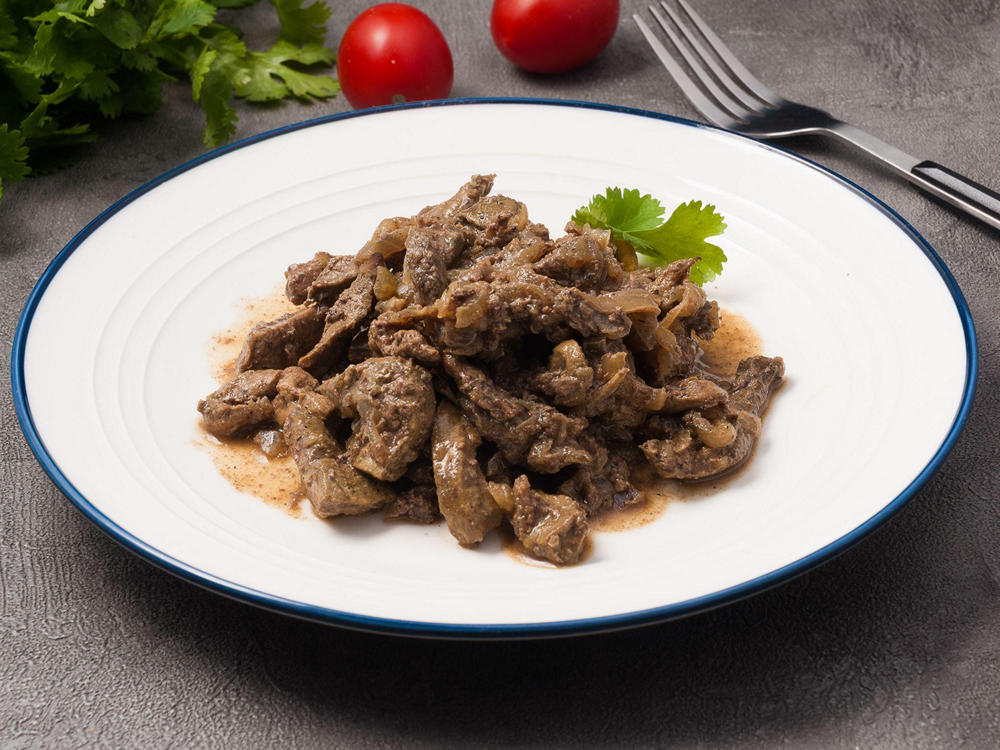 Бефстроганов из говядины На столе тарелка с готовым блюдом: бефстроганов из говядины, украшенный зеленью петрушки