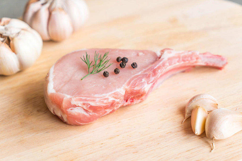 На столе небольшой кусок сырой баранины, украшенный горошинами перца и укропом