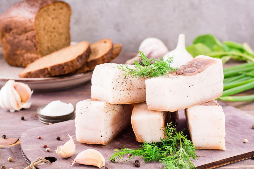 На доске куски сала, украшенные укропом, горошинами перца и чесноком