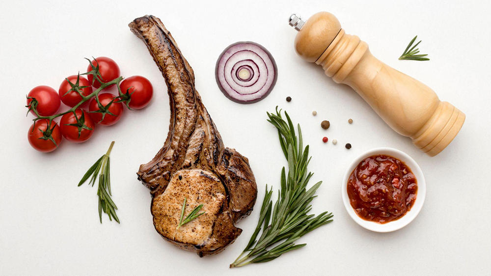 Готовое мясо баранины Готовый кусок баранины, лук, помидоры, соус и деревянная мельница для перца на белом фоне