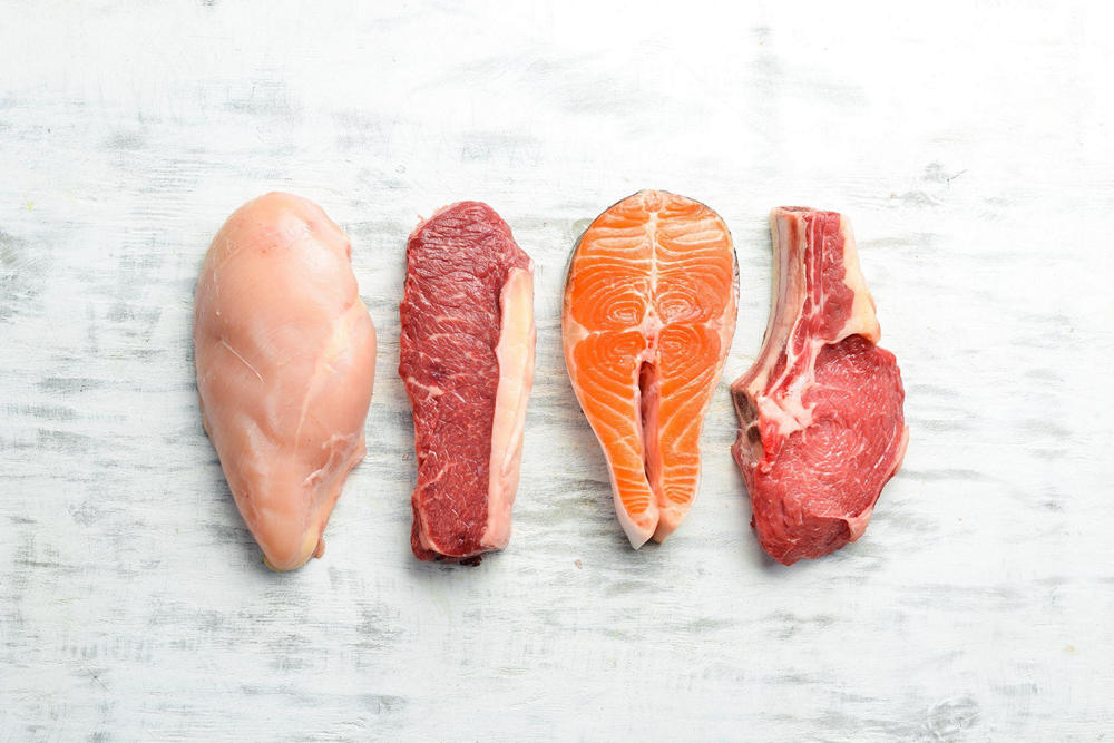Четыре куска мяса на столе: курица, говядина, красная рыба и свинина